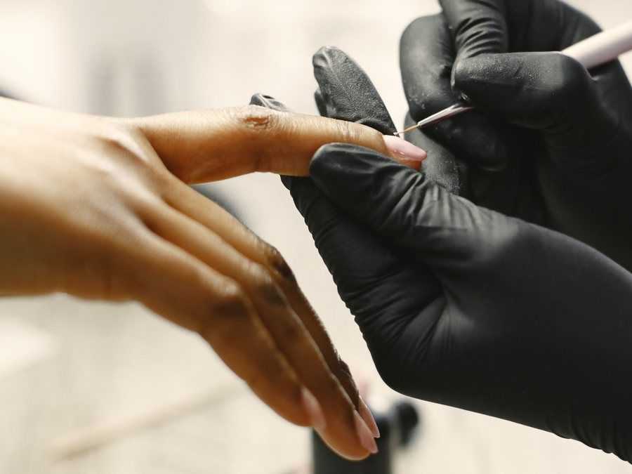 Manicura con guantes negros pintando con pincel fino una uña nude, belleza de manos