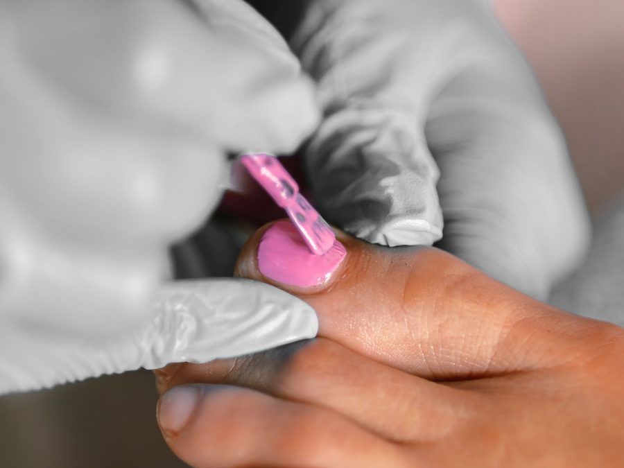 Manicura con guantes esmaltando de rosa la uña del pie, belleza de pies
